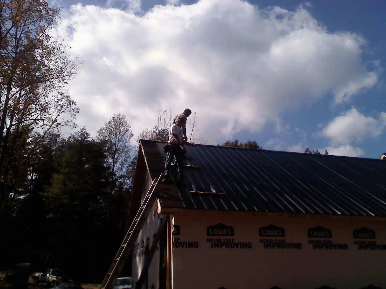 Roofer fastening dark metal panels high against a cloudy sky, from a Roof Inspection job in Blanding