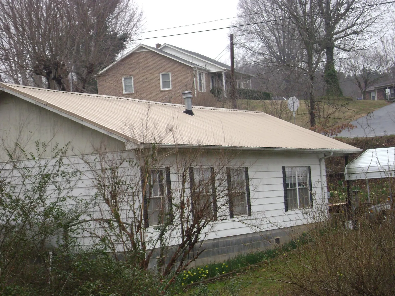 Tan metal roof on a white sided house set into a hillside — Commercial Roofing by Roofing Brothers in Blanding